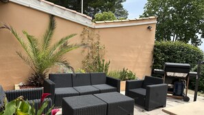 An outdoor patio with wicker furniture, a barbecue grill, and potted plants. - Campanile Manosque (Manosque)