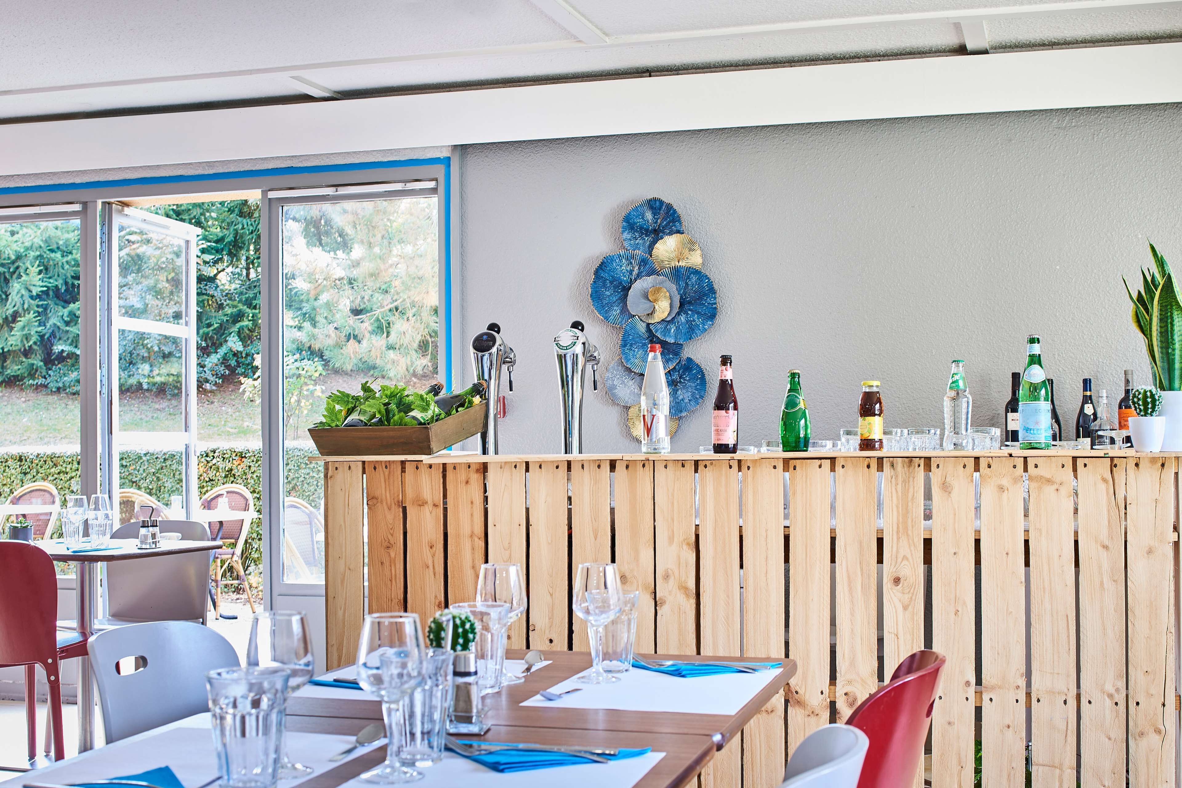 A restaurant with wooden paneling, a bar area with various bottles, and a large window offering a view of greenery.