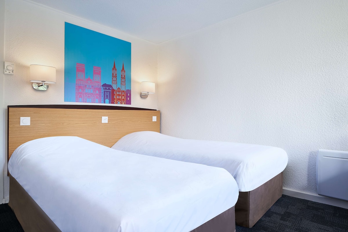 A hotel room with two beds, a cityscape painting on the wall, and two wall-mounted lamps.