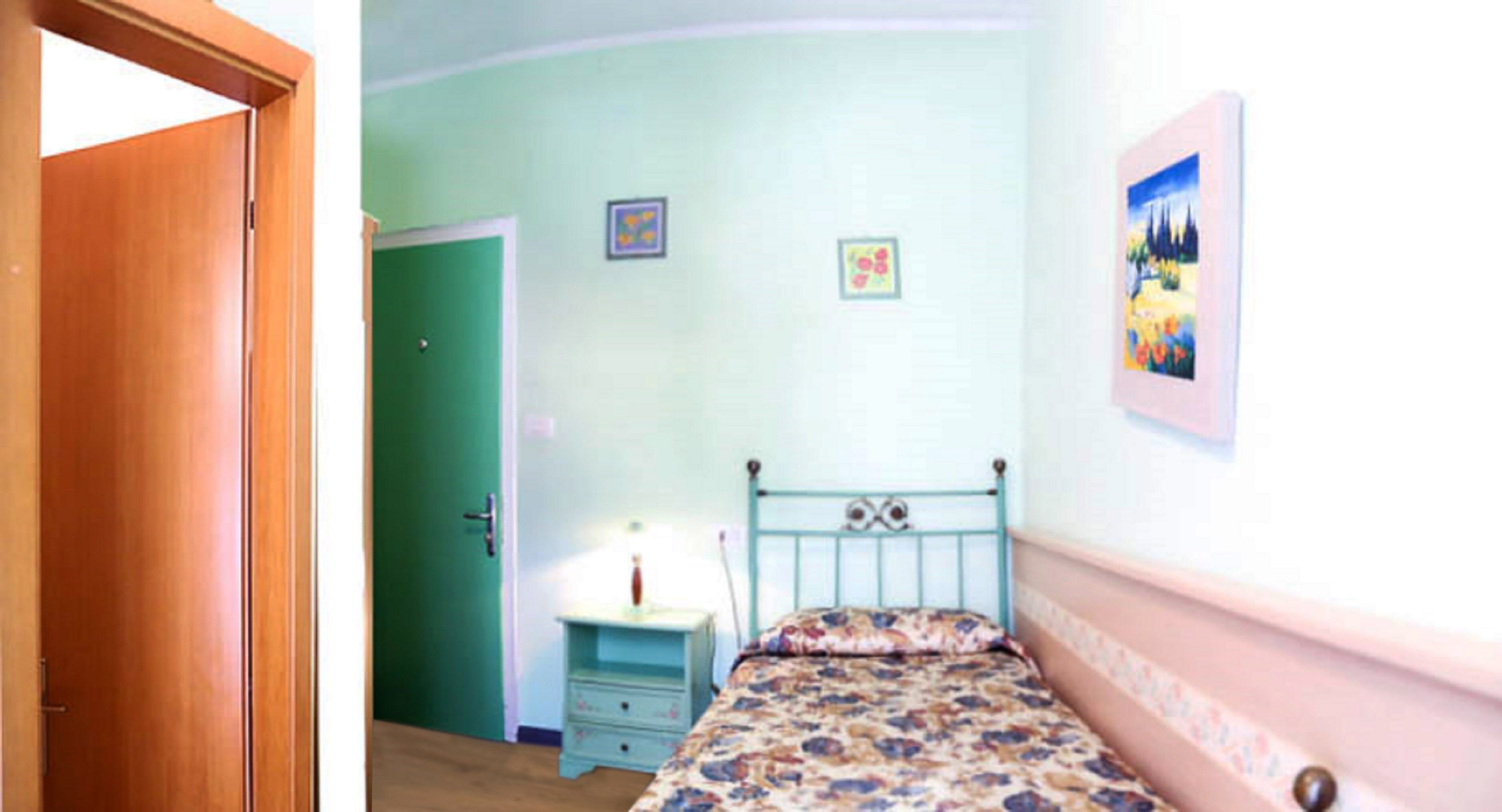 Ein Schlafzimmer mit einem Einzelbett, einem Nachttisch, einer grünen Tür und einer Wand mit zwei gerahmten Bildern.