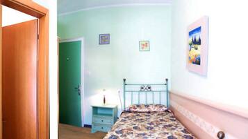 Ein Schlafzimmer mit einem Einzelbett, einem Nachttisch, einer grünen Tür und einer Wand mit zwei gerahmten Bildern.