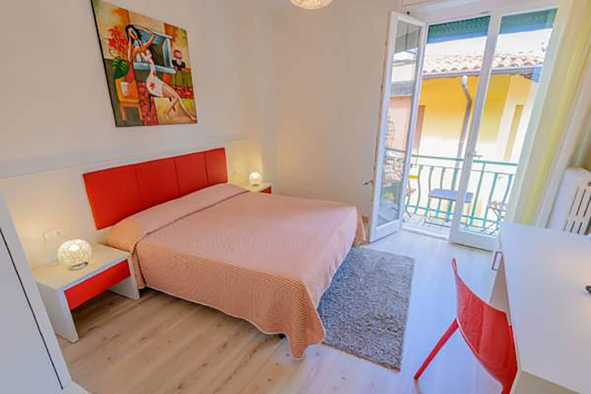 A bedroom with a bed, nightstands, a painting, and a balcony.