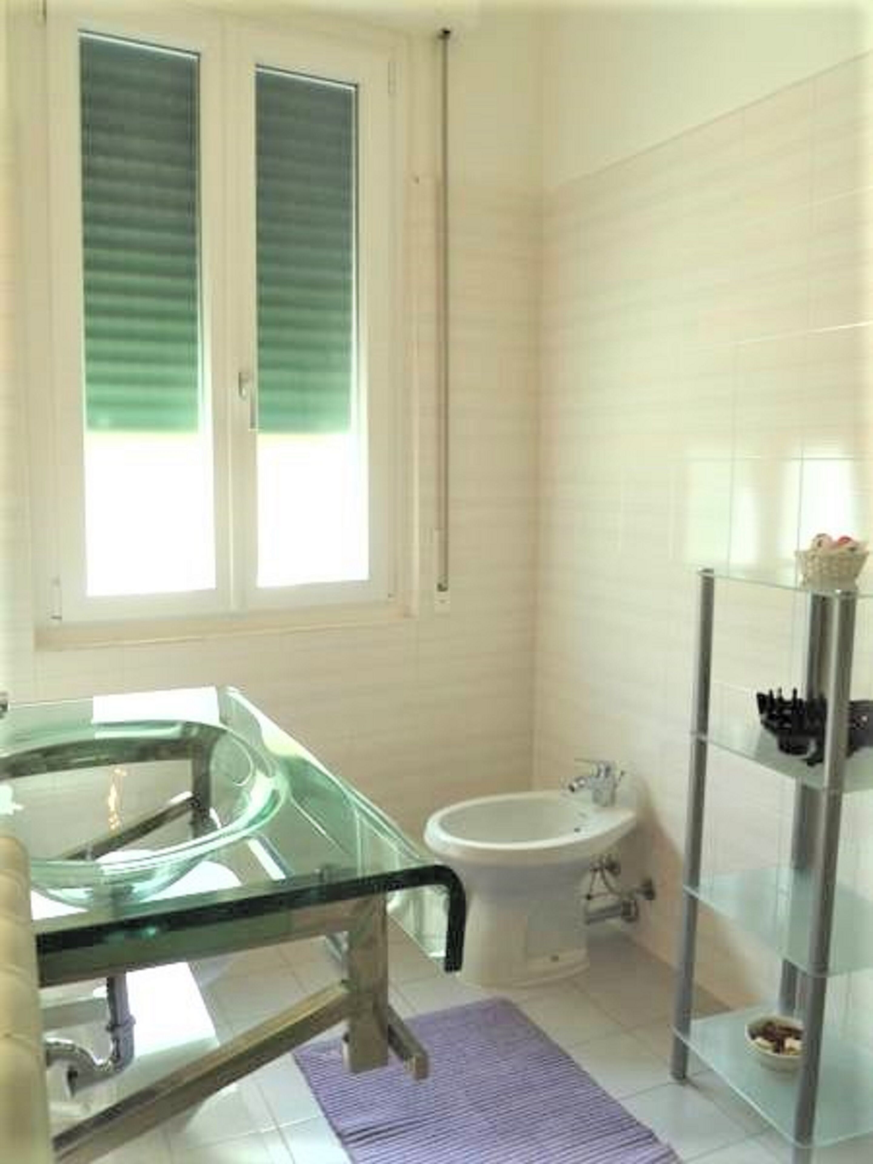 Une salle de bain avec une baignoire en verre, des toilettes blanches et une étagère en verre.