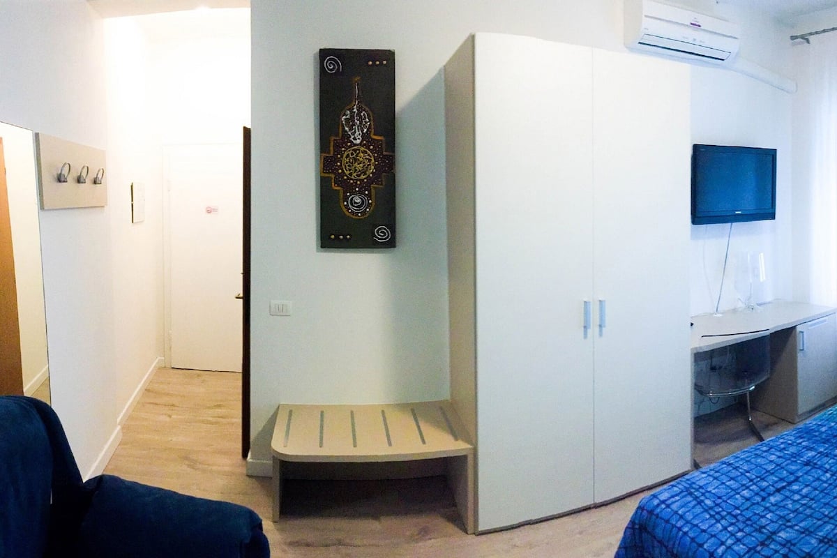A bedroom with a bed, a desk, a TV, and a wardrobe.
