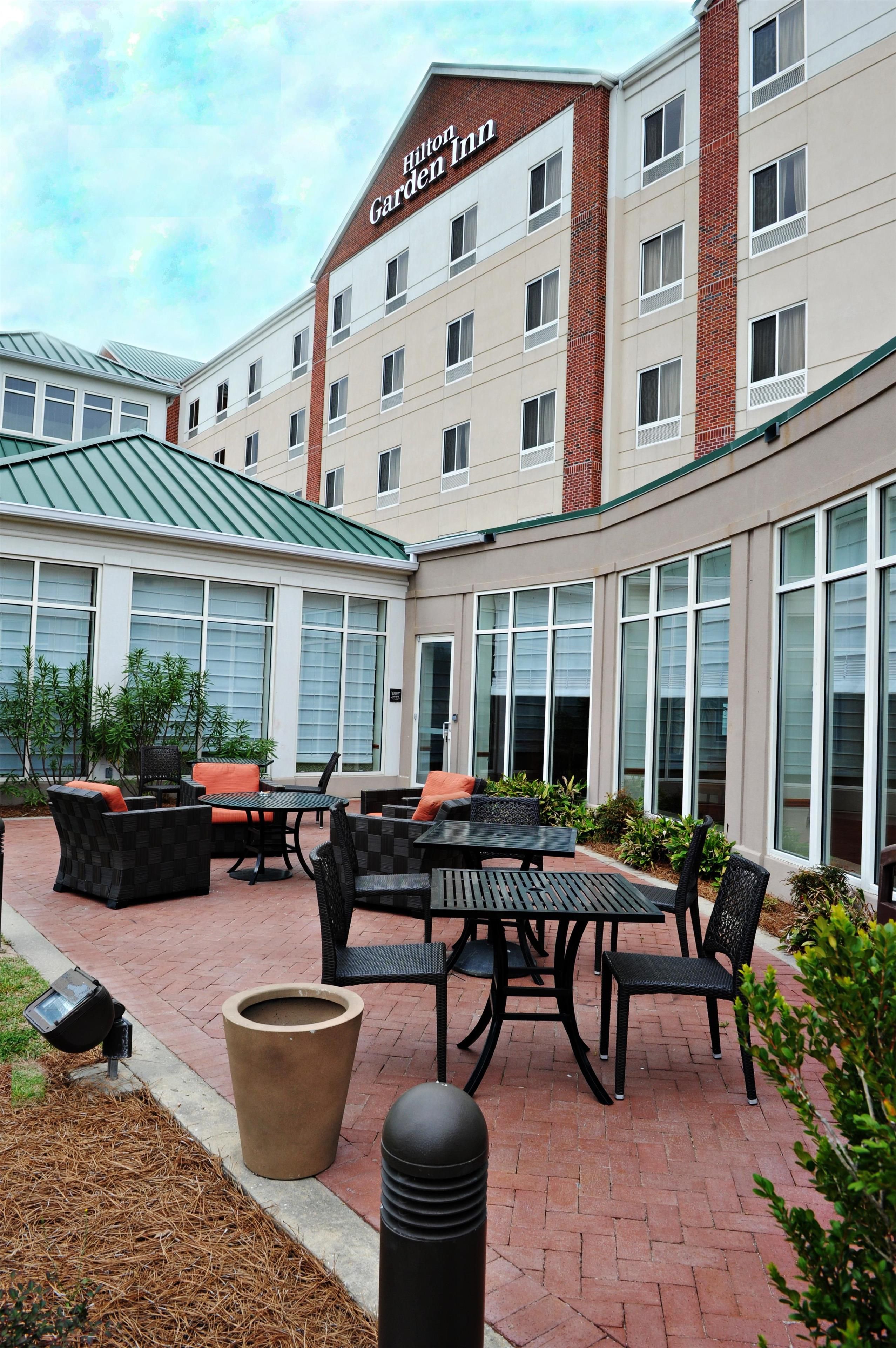 A hotel exterior with a patio area featuring outdoor furniture and a large planter.