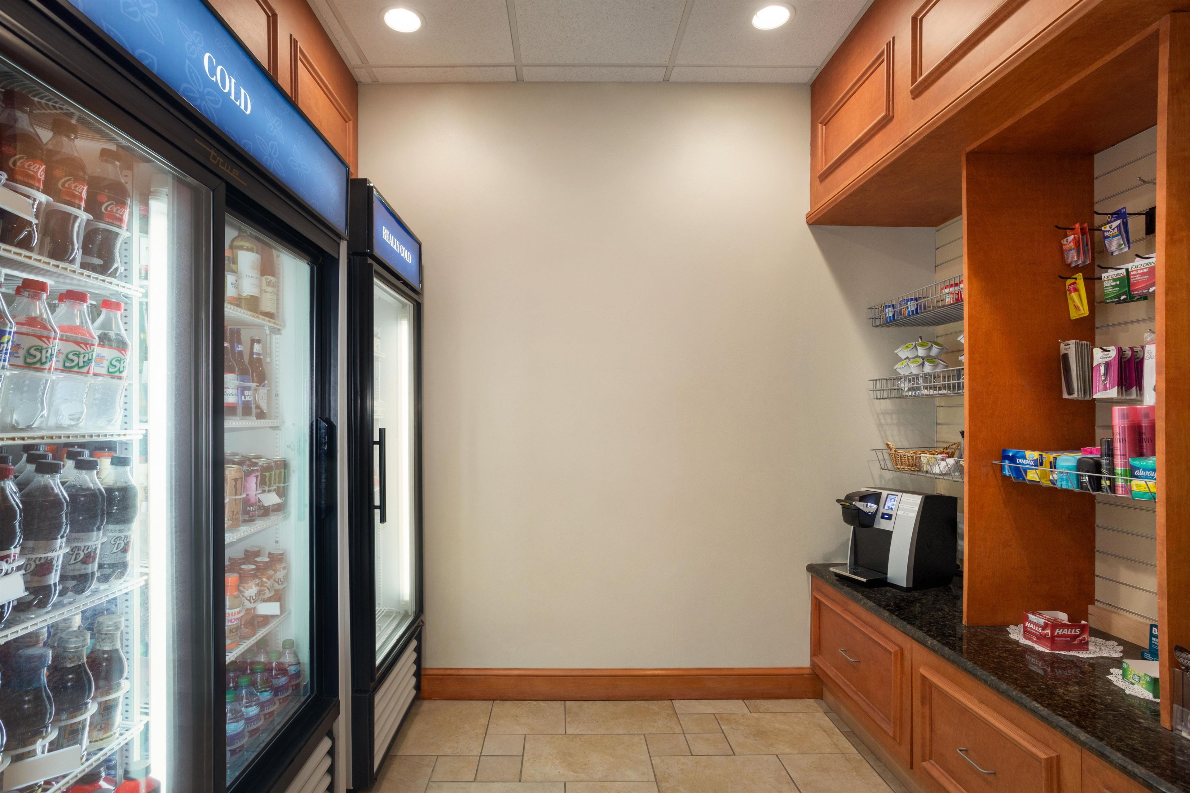 A small kitchenette with a refrigerator stocked with beverages, a coffee machine, and a shelf with toiletries.