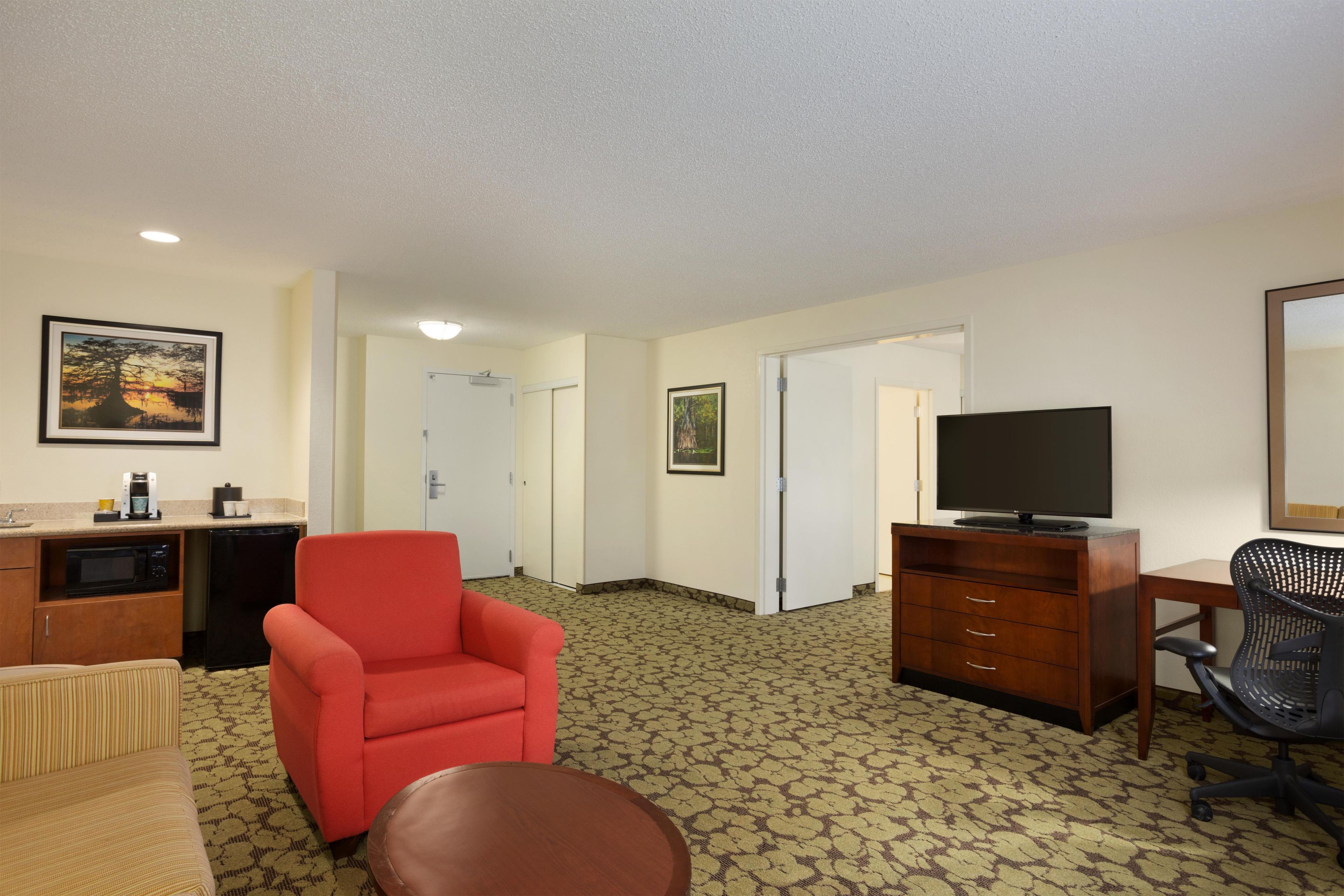 Una habitación de hotel con kitchenette, un sillón rojo, un televisor, un escritorio y una alfombra estampada.