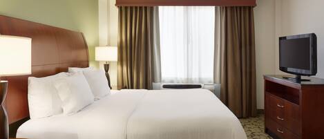 Una habitación de hotel con una cama grande, un televisor sobre un aparador de madera y una ventana con cortinas.