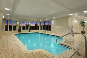 Une piscine intérieure avec des parois en verre transparent, un sol carrelé et un escalier métallique pour accéder au bassin.