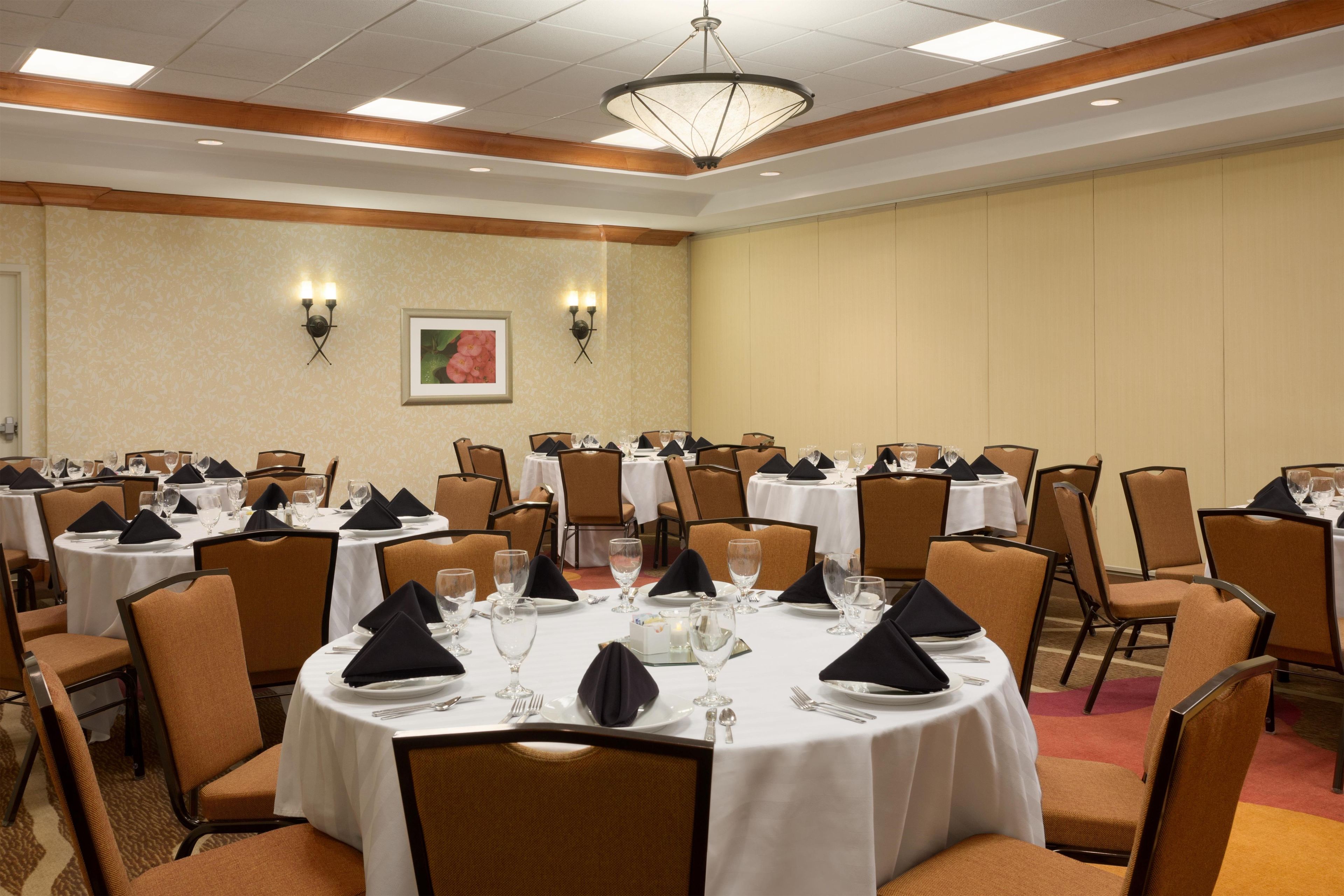 A conference room with multiple round tables, each set with white tablecloths, black napkins, and clear glassware.