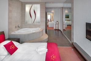 Una habitación de hotel moderna con una cama grande, una zona de estar separada, una bañera y un televisor.