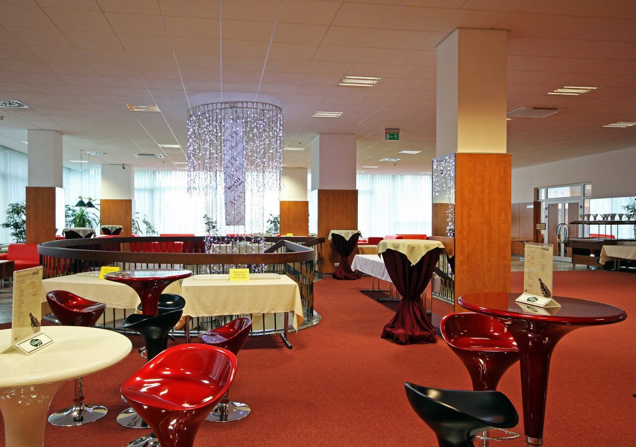 Een modern restaurant met ronde tafels en rode stoelen, met een bar in het midden en een decoratieve hanglamp.