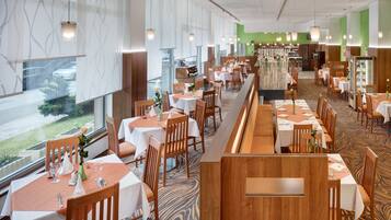 A restaurant with multiple tables and booths, large windows, and a patterned carpet.