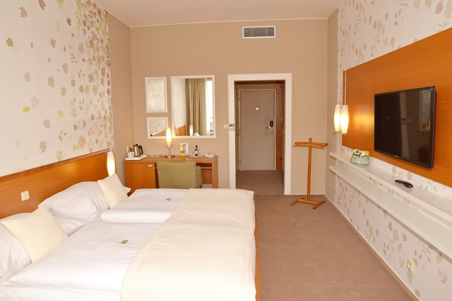 Une chambre d’hôtel avec deux lits, un bureau, une télévision et un miroir.