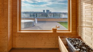 A wooden sauna room with a large window, a stone basin, and a wooden tub filled with rocks. - Avanti Hotel Brno (Brno)
