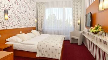 A hotel room with a large bed, a chair, a TV, and a flower vase.