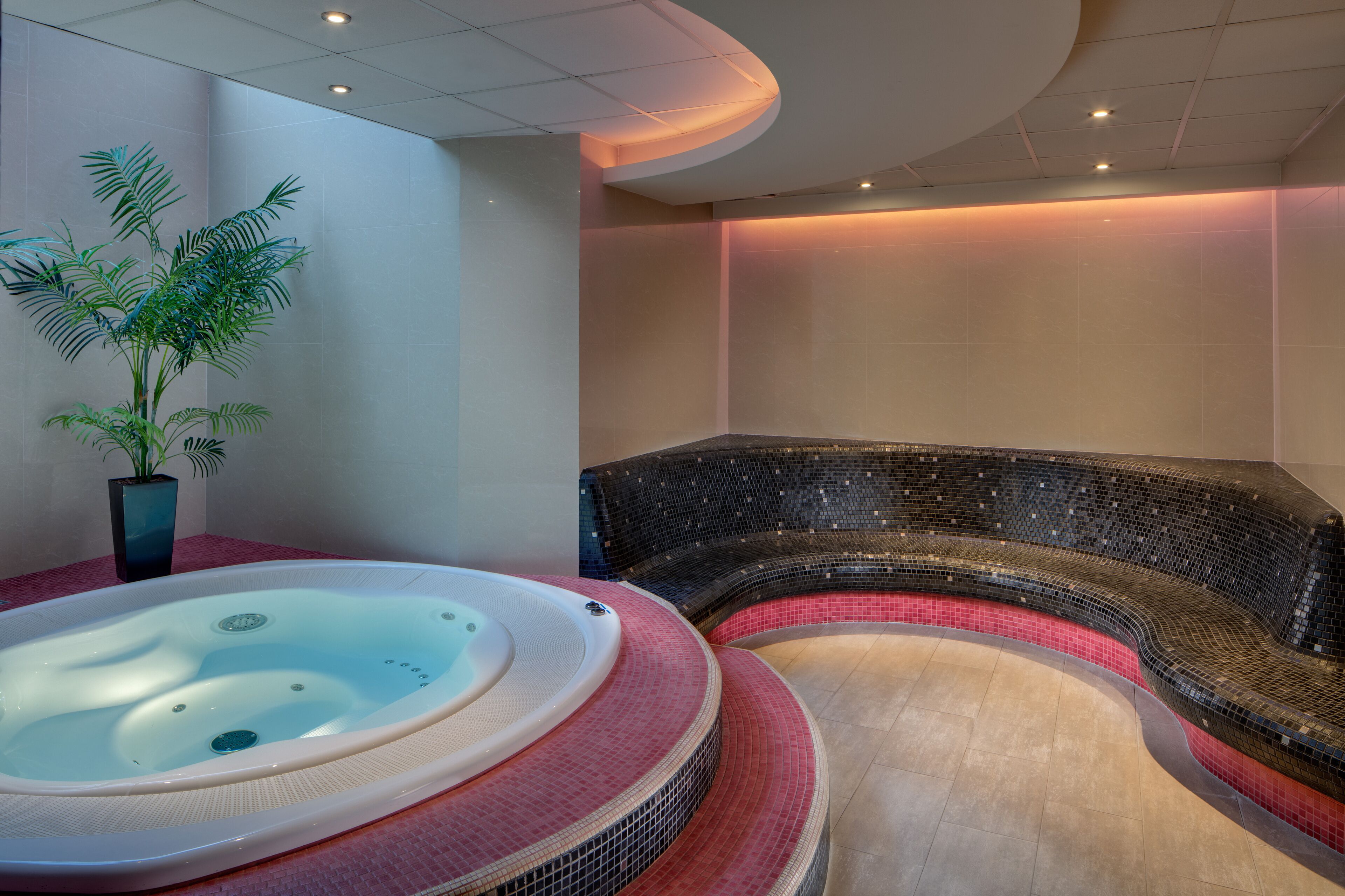 Ein Wellnessbereich mit Whirlpool und einer gebogenen Sitzecke mit Mosaikfliesen.