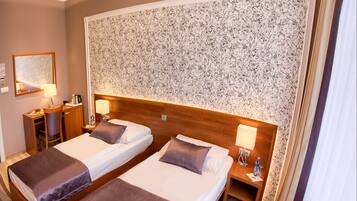 A hotel room with two beds, a desk, a chair, a mirror, and a floral wallpaper.