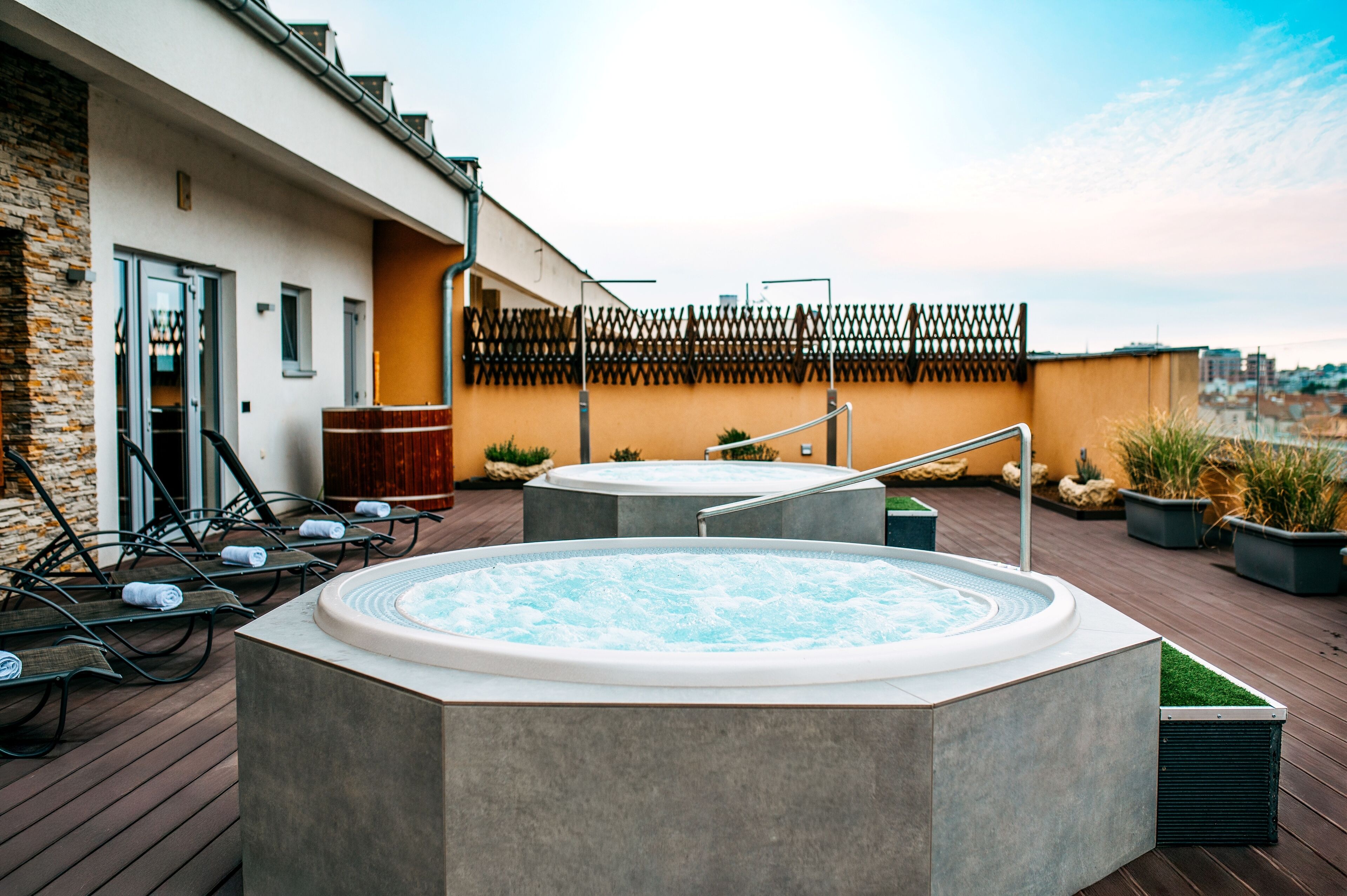 Una terraza en la azotea con dos jacuzzis, sillones de descanso y una valla de madera.