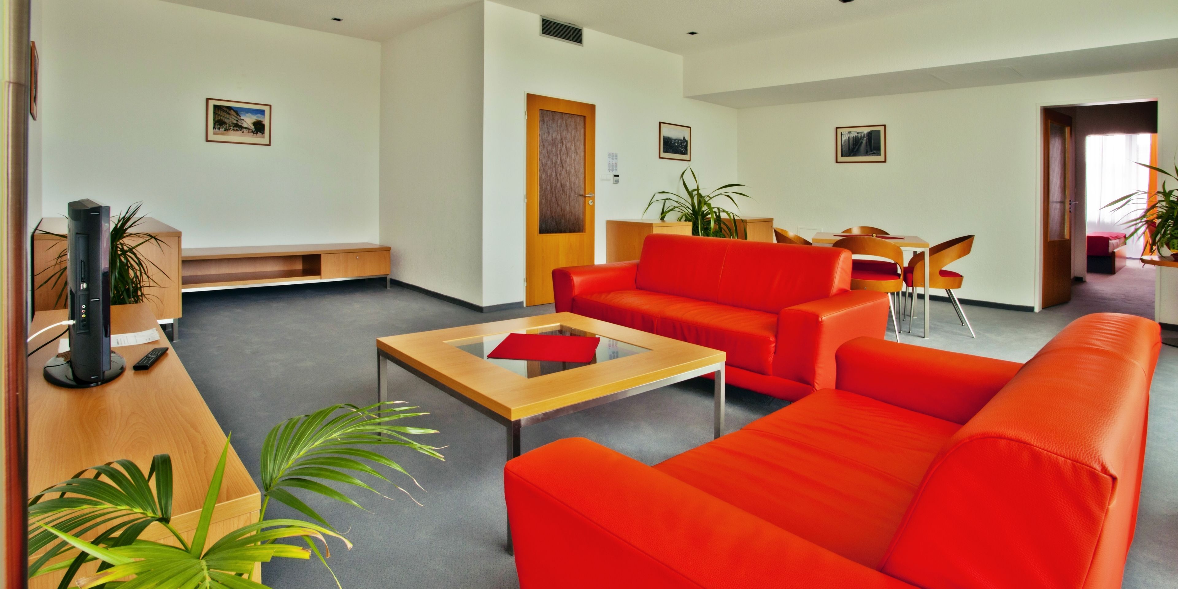 A modern living room with a red sofa, a wooden coffee table, and a desk with a computer and a plant.