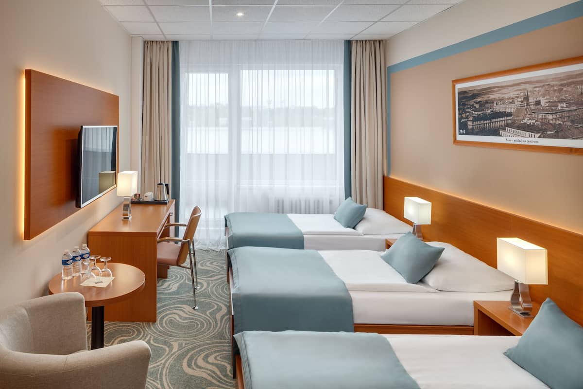 A hotel room with two beds, a desk, a chair, a TV, and a large window with curtains.