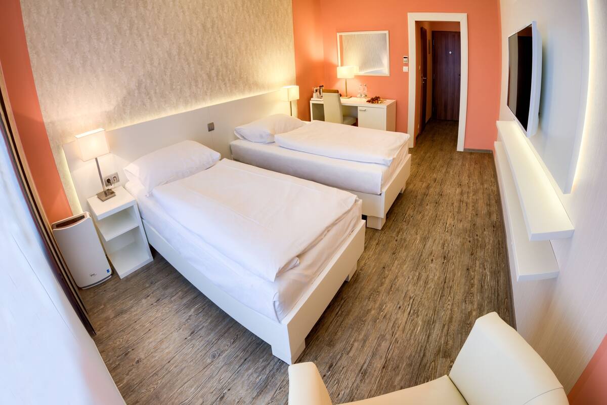 A hotel room with two beds, a chair, a desk, a TV, and a bathroom.