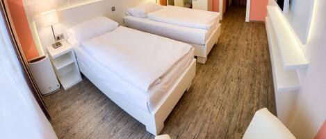 Quarto de hotel com duas camas, uma cadeira, uma escrivaninha, televisão e banheiro.