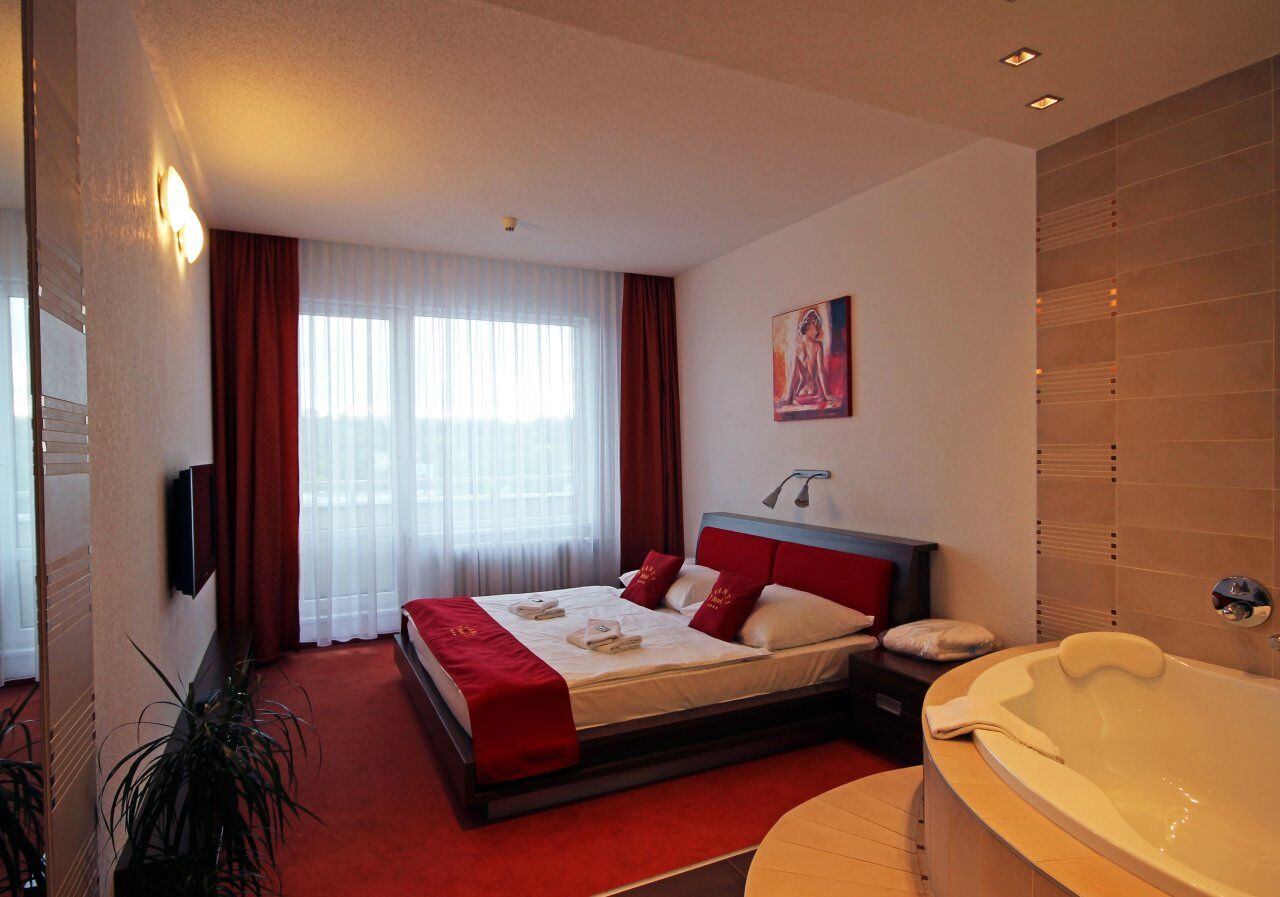 A hotel room with a large bed, a separate bathroom with a bathtub, and a television mounted on the wall.