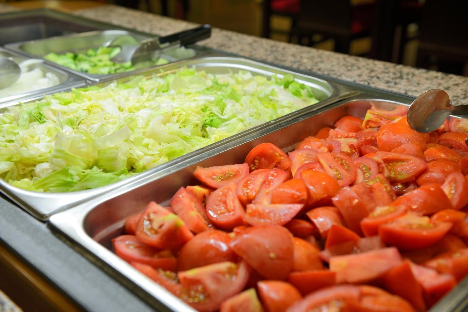 A buffet with various food options including sliced tomatoes and shredded lettuce.