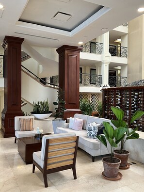 A spacious lobby with a staircase, a seating area with a sofa and armchairs, and potted plants.