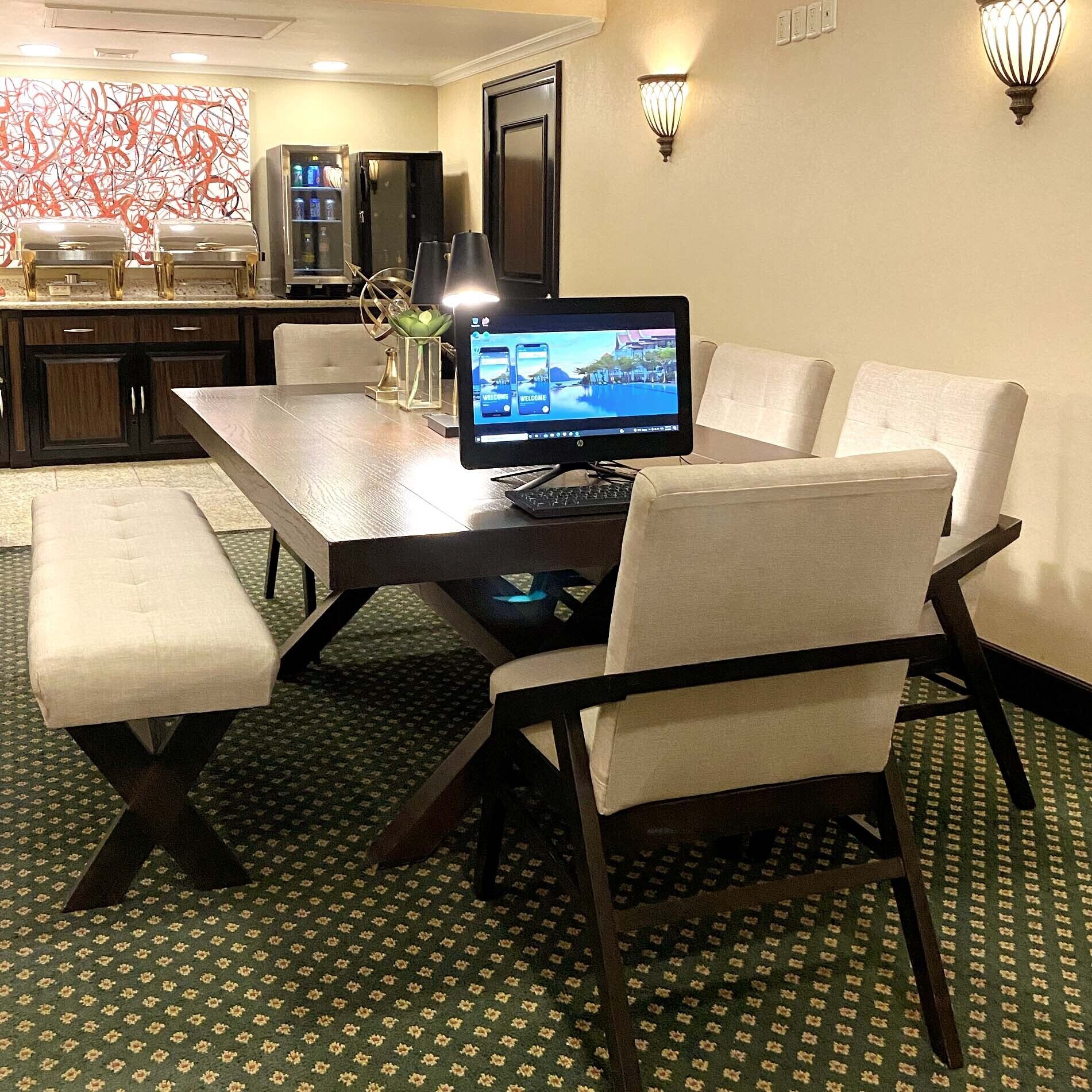 Habitación de hotel con mesa de comedor, cuatro sillas, una computadora portátil, un ordenador de escritorio, un refrigerador, un minibar y un elemento decorativo en la pared.