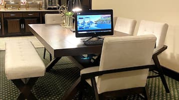 Habitación de hotel con mesa de comedor, cuatro sillas, una computadora portátil, un ordenador de escritorio, un refrigerador, un minibar y un elemento decorativo en la pared.