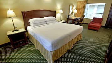 A hotel room with a large bed, two bedside tables with lamps, a desk with a chair, and a view of the outside through a window.