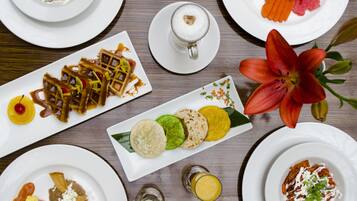 Variedad de platos sobre una mesa de madera, incluyendo gofres, fruta y una flor.