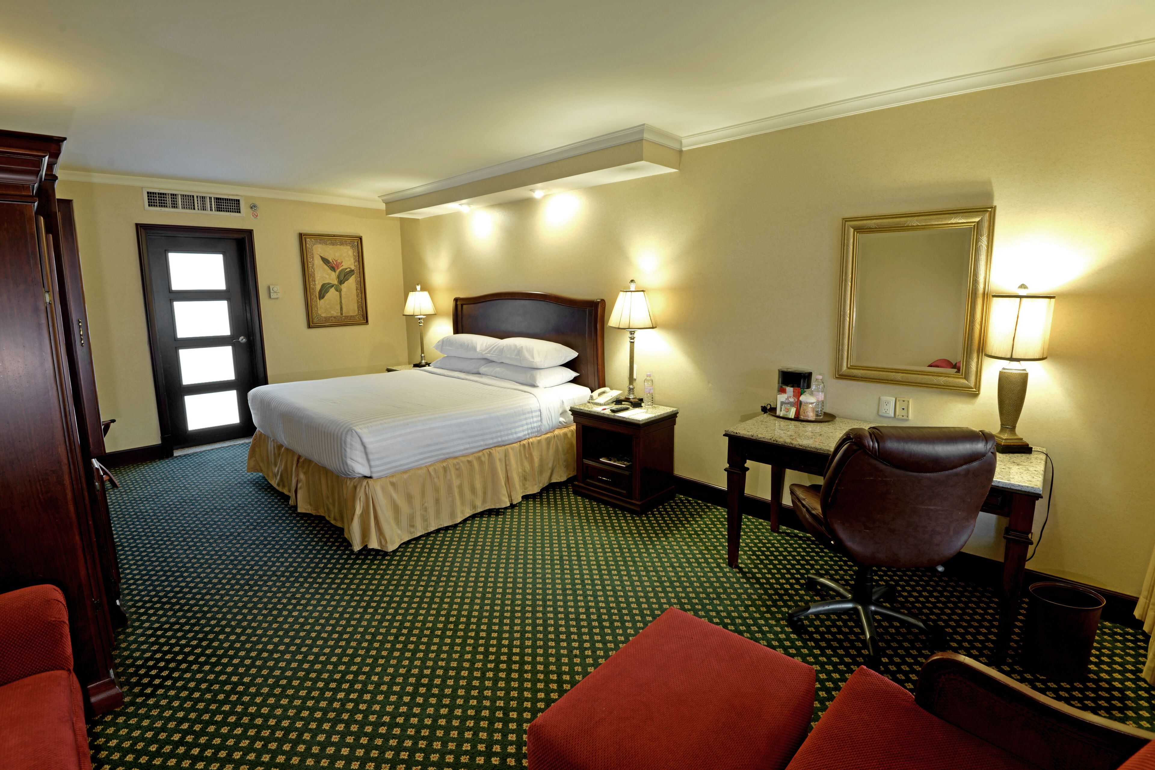 Una habitación de hotel con cama, dos mesitas de noche, un escritorio, una silla y un espejo grande.