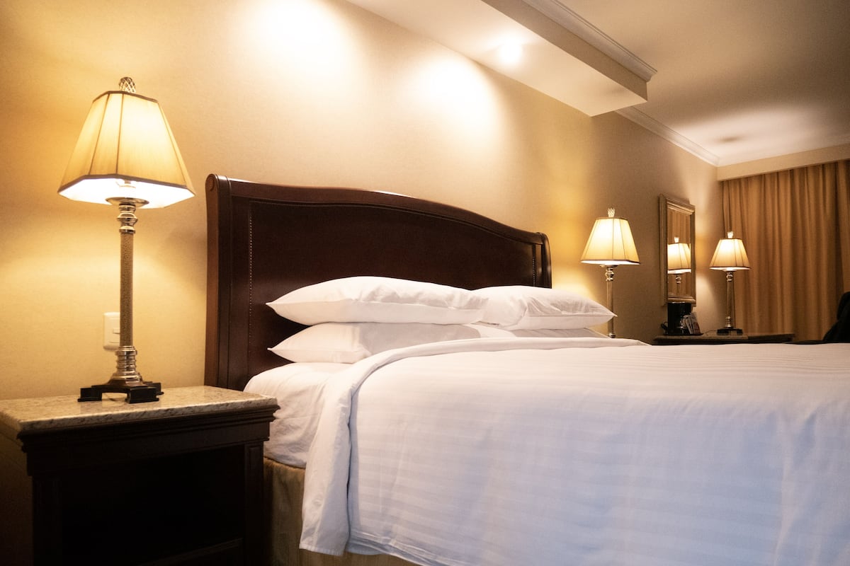 A hotel room with a neatly made bed, a nightstand with a lamp, and a mirror on the wall.