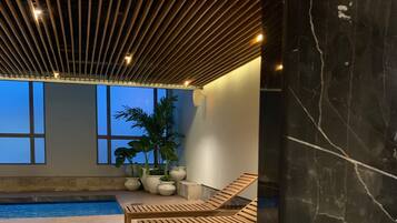 A poolside area with wooden loungers, a tiled floor, and a ceiling with wooden slats.