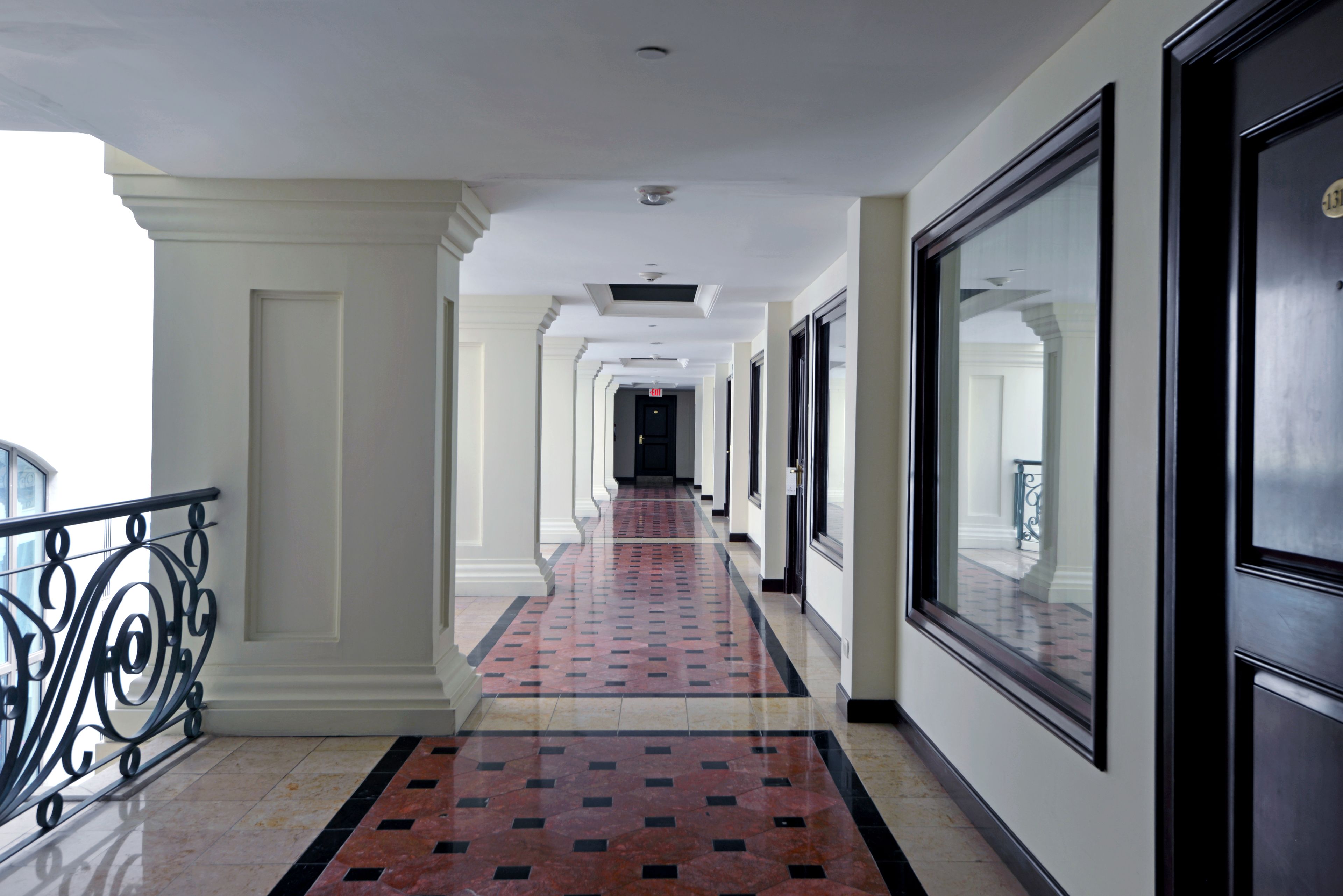 A hotel corridor with a tiled floor, white walls, and black-framed doors.