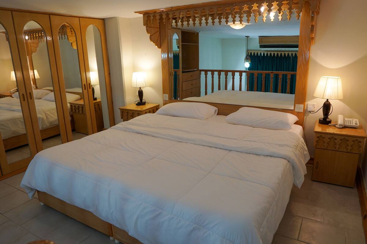 A large bed with a canopy, wooden nightstands with lamps, and a mirror cabinet.