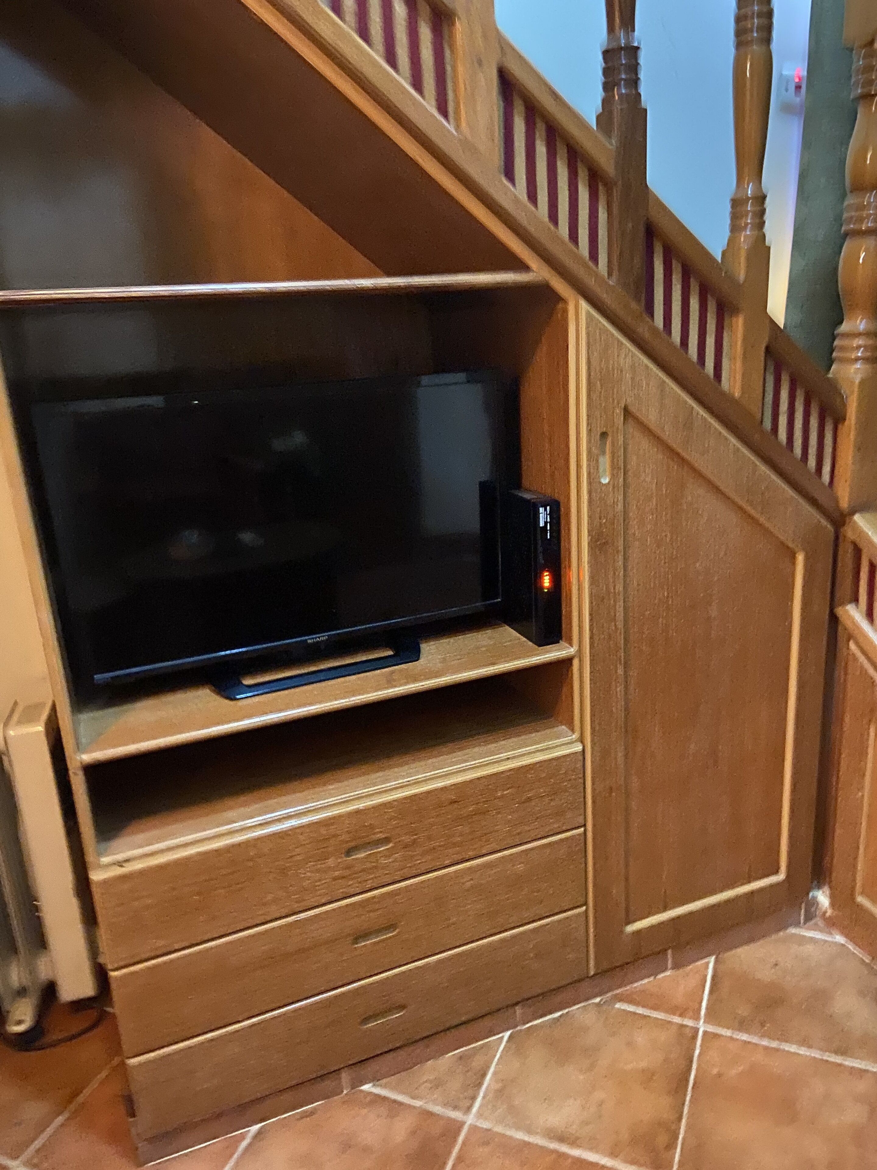 A wooden entertainment unit with a flat-screen TV, a small speaker, and a drawer.