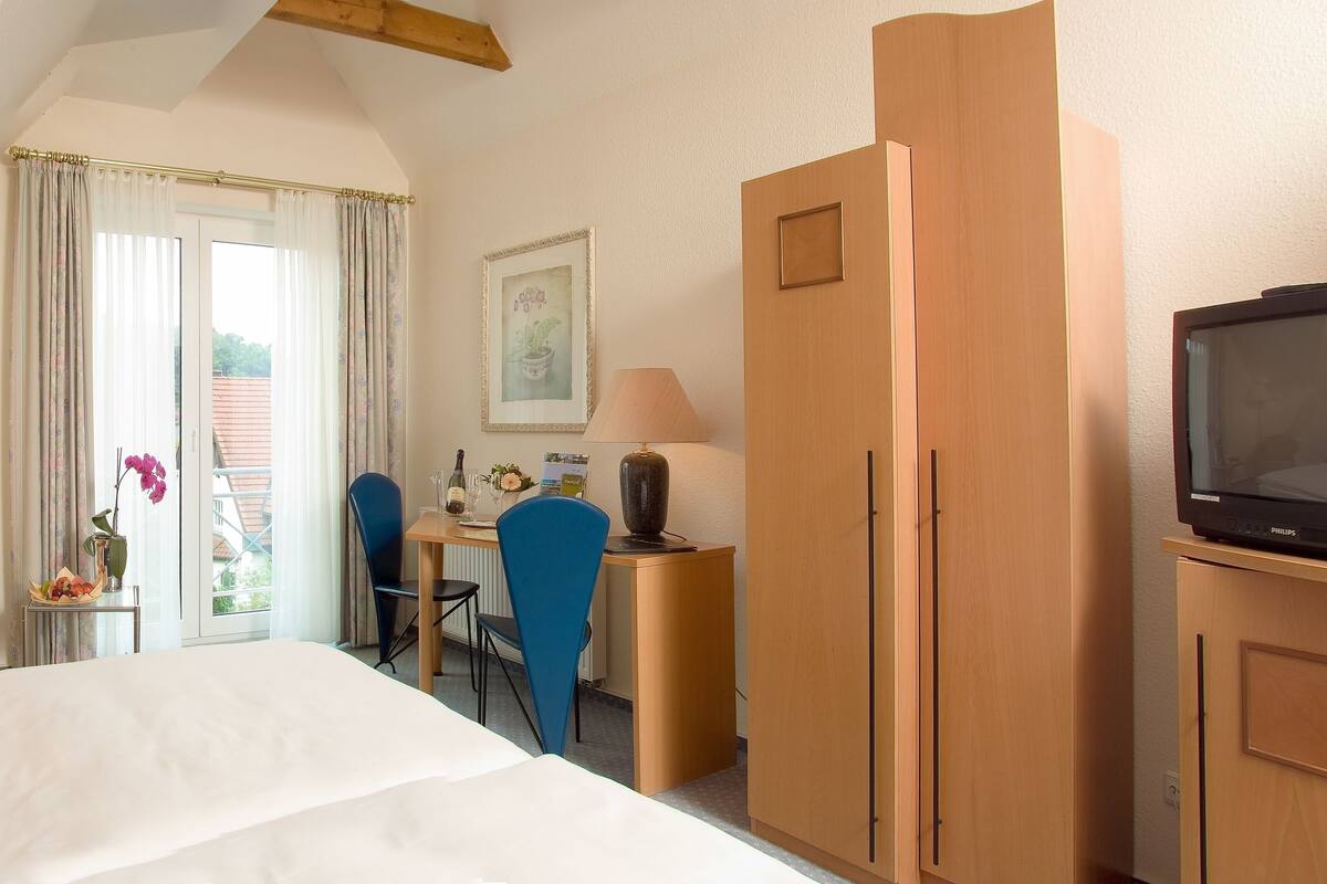 A hotel room with a bed, a desk with a chair, a television, and a window with curtains.