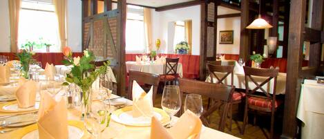 Un restaurante con mesas dispuestas para comer, con servilletas dobladas con cuidado, copas de vino y diferentes tipos de colocación de mesa.