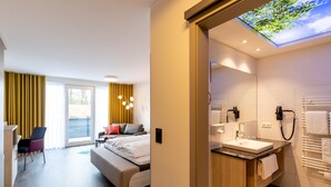 A modern hotel room with a bed, a desk, a chair, and a bathroom with a sink and mirror. - Hotel Leugermann (Ibbenbueren)