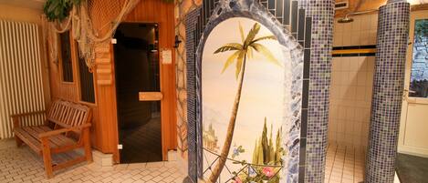 Un baño con suelo de baldosas, una banca de madera y un mural de una palmera.