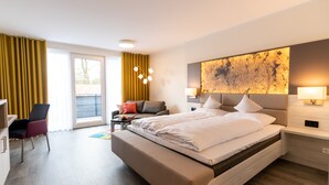 A modern hotel room with a large bed, a desk, a chair, and a sofa. - Hotel Leugermann (Ibbenbueren)