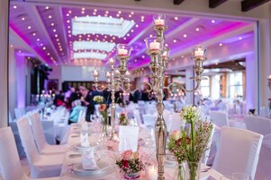 Un salón de banquetes con mesas dispuestas para un evento formal, con candelabros y centros de mesa florales.