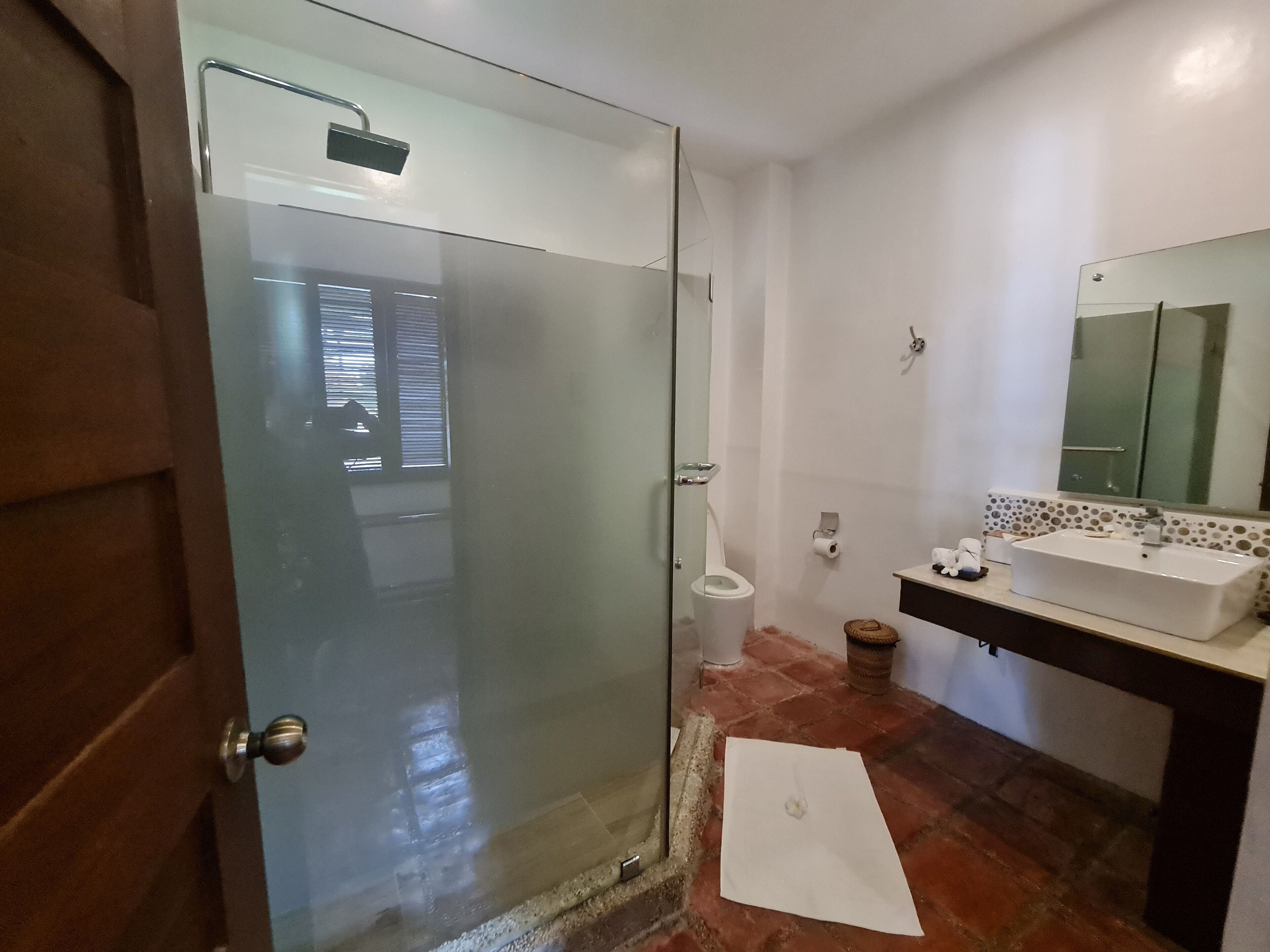 Ein Badezimmer mit Glasduschtür, Toilette, Waschbecken inklusive Spiegel und gefliestem Boden.