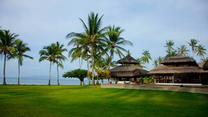 A resort with thatched-roof structures, palm trees, and a grassy area by the sea. - The Ananyana Beach Resort by SMS Hospitality (Panglao)