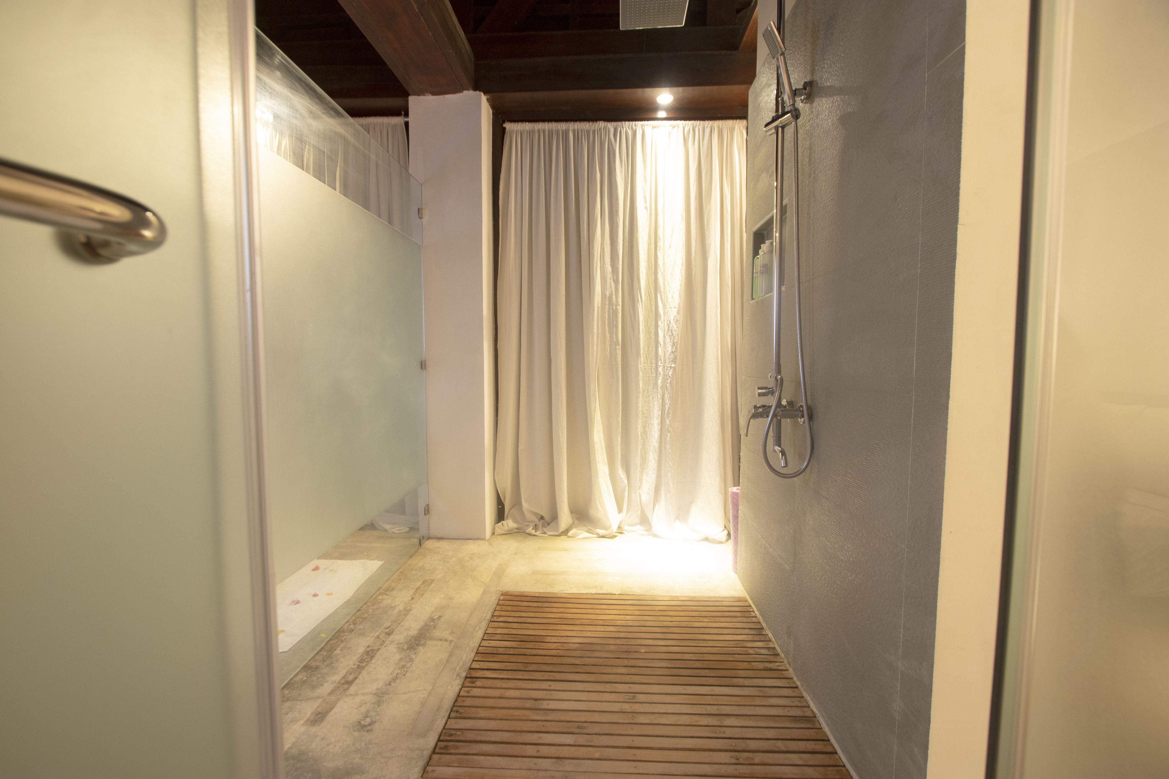 A narrow hallway with a wooden floor, a shower area with a glass door, and a curtain.