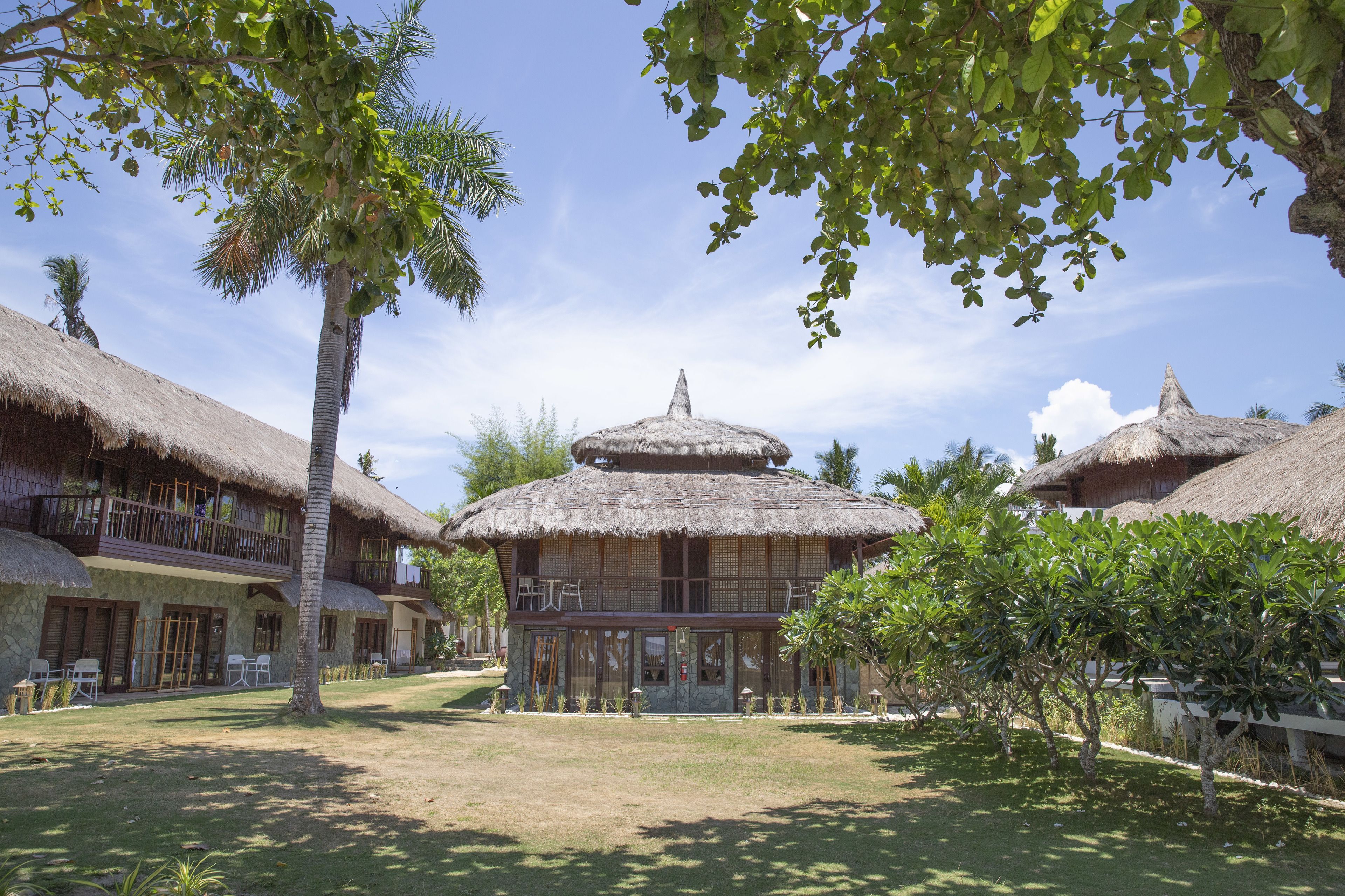 Un resort con edificios de techo de paja, una estructura central con cúpula y un césped bien cuidado.